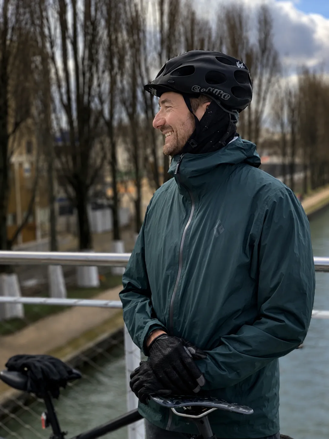 Steph, casque sur la tête, sourit sur une passerelle au-dessus d'un canal, la main posée sur la selle de son vélo — réparateur vélo dans le 13e arrondissement — The Rolling Steph
